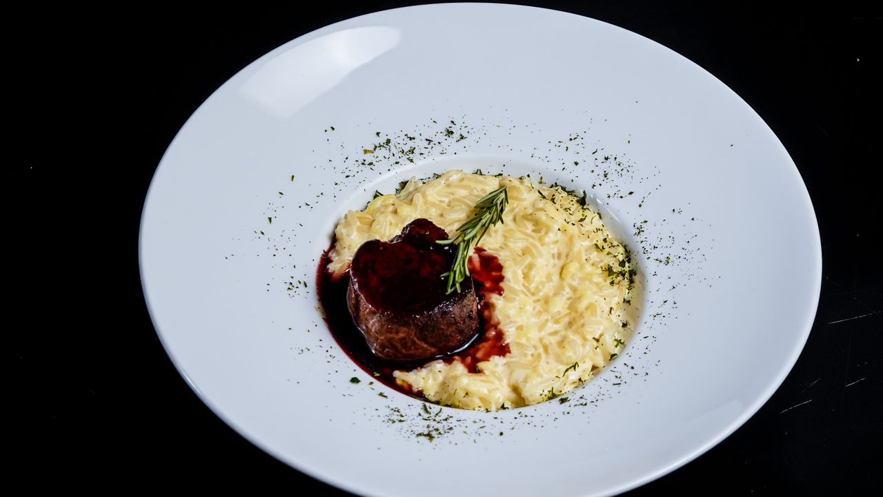 Delicious beef fillet with red wine reduction and creamy risotto on a white plate.