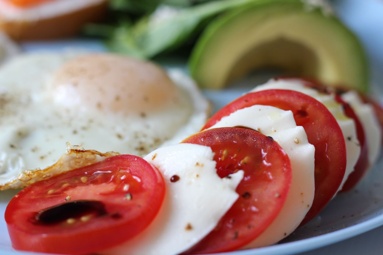 Close-up of a delicious caprese salad with fresh tomato, mozzarella, avocado, and a sunny-side-up egg.